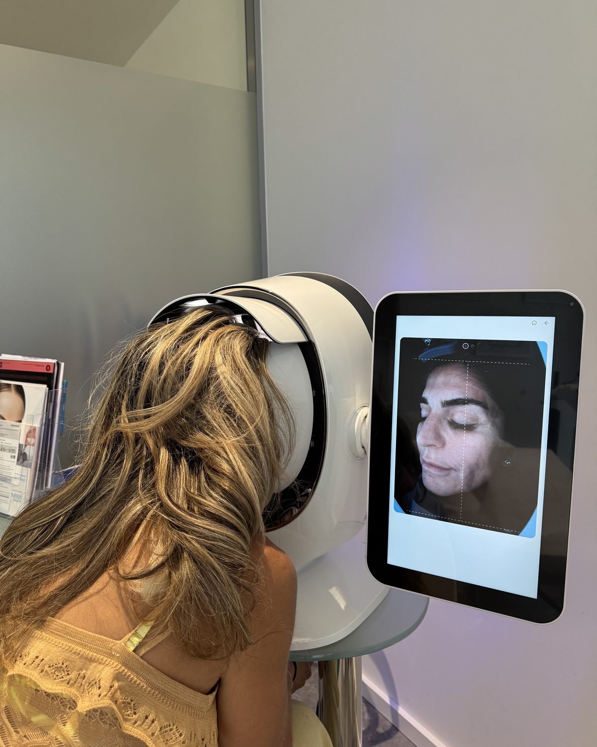 Une cliente installée au scanner de peau ; l'écran affiche la photographie de son visage